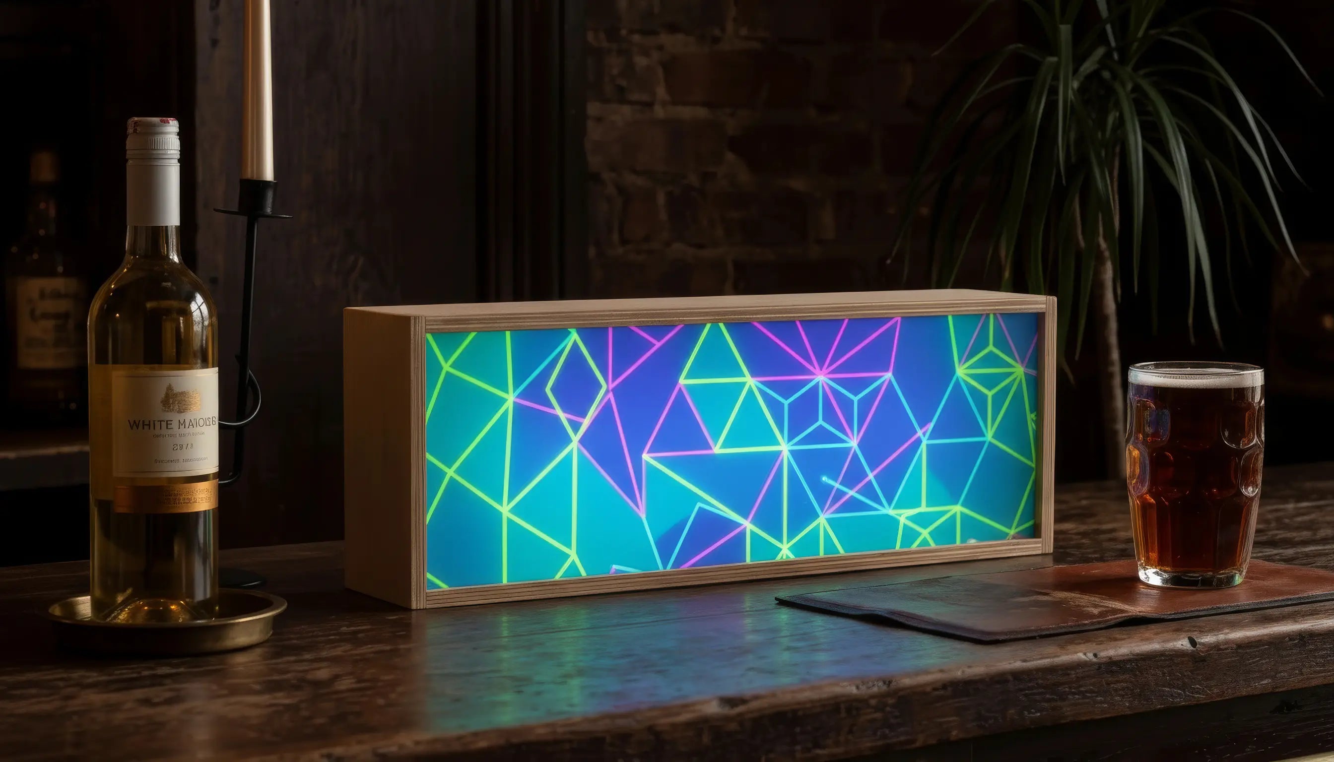 Colorful geometric LED light box on a wooden surface with a bottle of wine and a glass of beer in the background.
